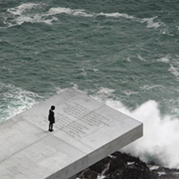 Joven de pie una pasarela de hormigón al borde del mar